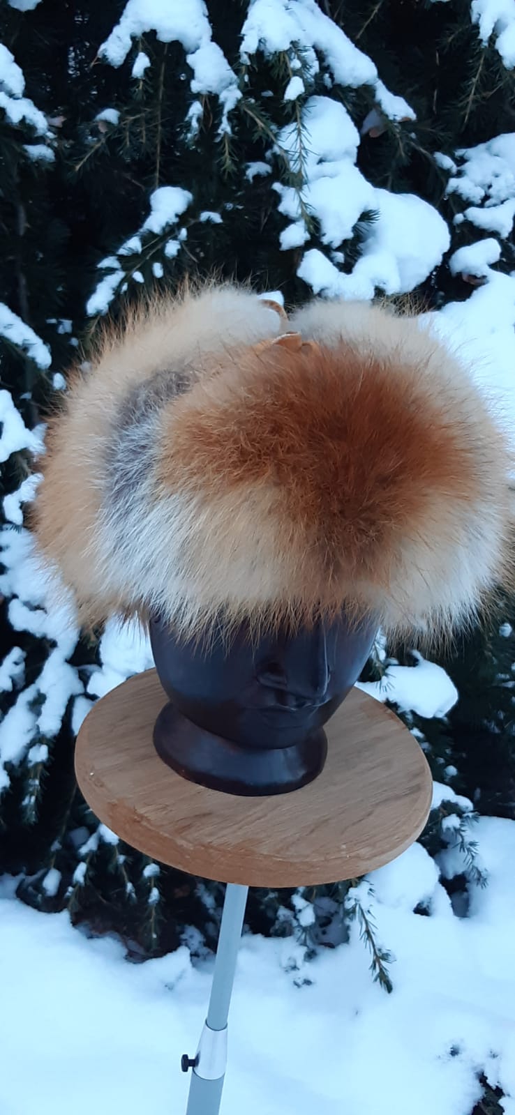 Fuchspelzmütze auf Schaufensterbüste vor verschneitem Nadelbaum